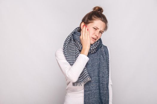 Sick woman holding hand her cheeh, have a toothache. Studio shot, gray wall