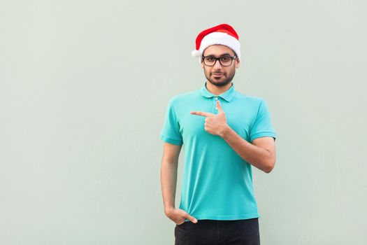 Businessman pointing copy space. Handsome man with beard in blue shirt looking at camera and pointing away while standing isolated on gray background. Studio shot