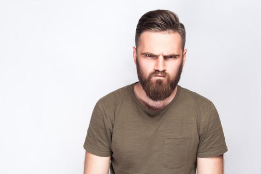 Portrait of angry sad bearded man with dark green t shirt against light gray background. studio shot. .