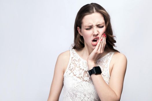Portrait of beautiful woman with freckles and white dress and smart watch with tooth pain on silver gray background. healthcare and medicine concept.
