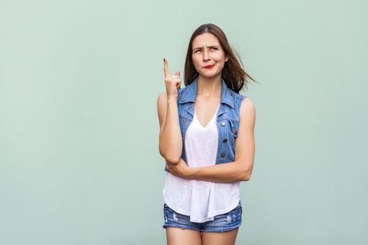 Pretty casual style girl with freckles got the idea and she raised her finger up and thinking. Isolated studio shot on light green background