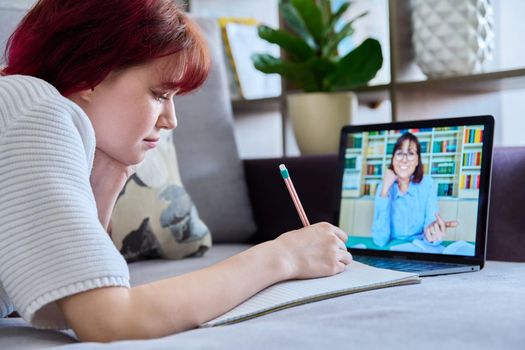 Teenage female student at home looking listening to online lesson, teacher on laptop screen. Virtual communication, video call chat conference. E-education, technology, adolescence, distance learning