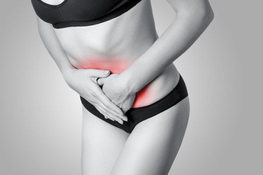 Closeup view of a young woman with stomach pain or digestion or period cycle on gray background. Black and white photo with red dot.