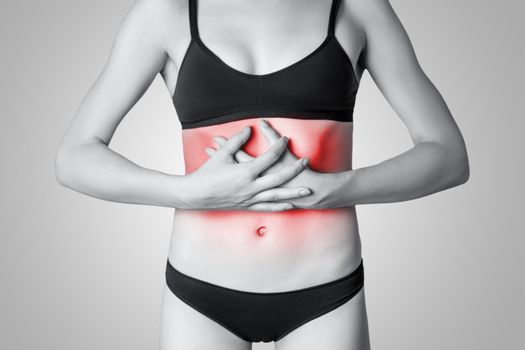 Closeup view of a young woman with stomach pain or digestion or period cycle on gray background. Black and white photo with red dot.