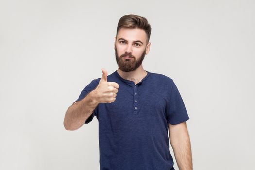 Happy bearded man showing thumb up and smile. Isolated studio shot on gray background