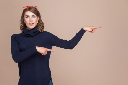 Emotional woman looking at camera and pointing fingers at copy space. Studio shot