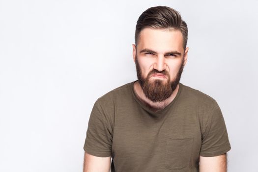 Portrait of angry sad bearded man with dark green t shirt against light gray background. studio shot. .