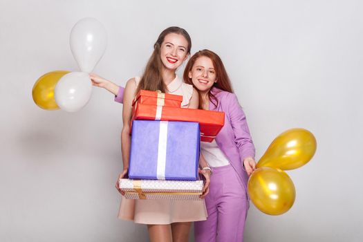 Two beautiful girl holding gifts box and air balloon have a happiness look and showing a v sign at camera. Studio shot