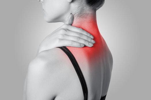 Closeup view of a young woman with shoulder or neck pain on gray background. Black and white photo with red dot.