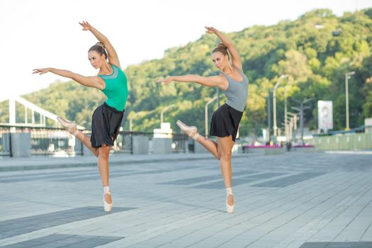 Two young beautiful twin sister dancing ballet in the city with ballet costume. urban sync dance. industrial street dancing. with special effect. synced posing. pointe ballet shoes and dress.