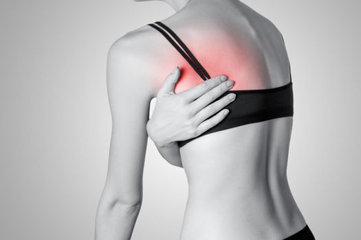 Closeup view of a young woman with pain in back on gray background. Black and white photo with red dot.