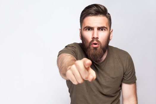 Hey You! Portrait of surprised excited bearded man with dark green t shirt against light gray background. studio shot. .