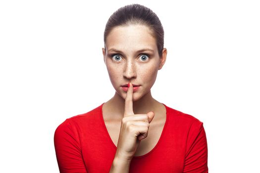 Portrait of serious woman in red t-shirt with freckles with shh sign on her lips. studio shot. isolated on white background.