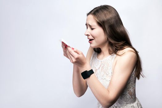 Portrait of sick cold woman with freckles and white dress and smart watch on silver gray background. healthcare and medicine concept.