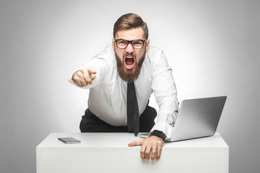 Portrait of aggressive unhappy young businessman in white shirt and black tie are blaming you in office and having bad mood, screaming and pointing finger at camera and screaming. Indoor, studio shot