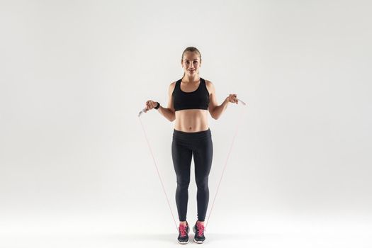 Happiness woman holding skipping rope, looking at camera and smiling. Studio shot, gray background