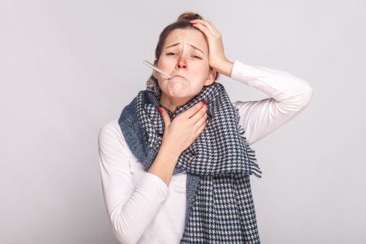 Young sick woman holding throat and head. Have a temperature. Studio shot, isolated on gray background