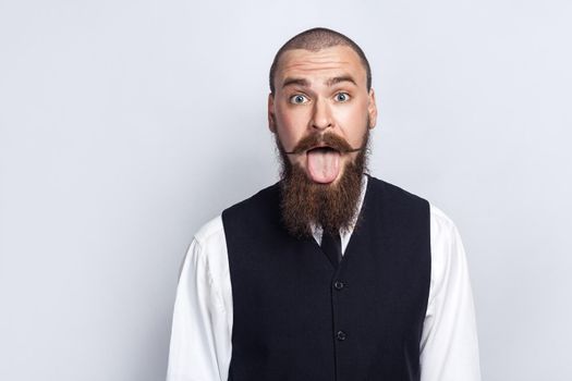 Crazy Funny face. Handsome businessman with beard and handlebar mustache looking at camera with tongue out. studio shot, on gray background.
