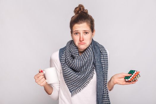 Worry puzzled woman holding cup with tea, many pills . Studio shot, isolated on gray background