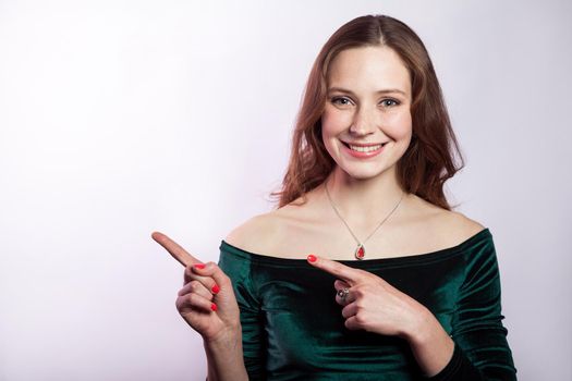 Portrait of beautiful happy woman with freckles and classic green dress showing empty space with finger. studio shot on silver gray background.