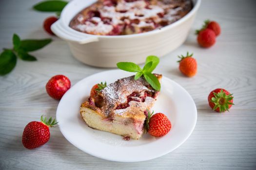 Sweet cottage cheese casserole with strawberry filling, in a plate on a wooden table.