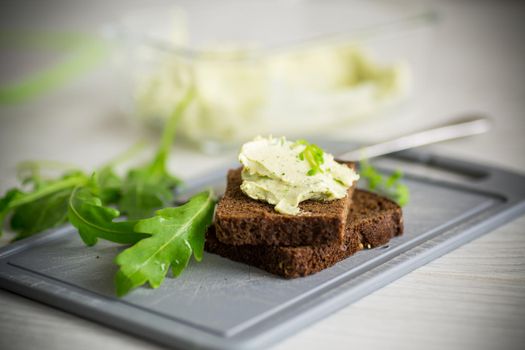 bread cheese spread with garlic and arugula on dark bread, on a wooden table.