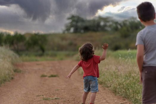 Two Caucasian boys walk through the field looking at a storm in the sky