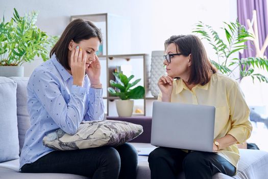 Upset sad young woman at session with psychologist. Mature female psychologist counseling helping patient, women sitting on couch in office. Psychology, psychiatry, treatment, mental health concept