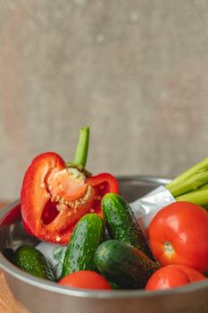 Vegetables lie in a metal bowl tomatoes, asparagus, cucumbers, red bell peppers . on a wooden board and brown background. back gray background. place for text.