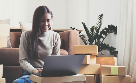 Startup small business entrepreneur or freelance Asian woman using a laptop with box, Young success Asian woman with her hand lift up, online marketing packaging box and delivery, SME concept..