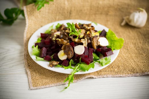 Salad with boiled beets, fried eggplants, herbs and arugula in a plate, on a wooden table.