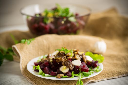 Salad with boiled beets, fried eggplants, herbs and arugula in a plate, on a wooden table.