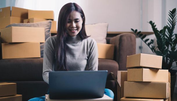 Startup small business entrepreneur or freelance Asian woman using a laptop with box, Young success Asian woman with her hand lift up, online marketing packaging box and delivery, SME concept..