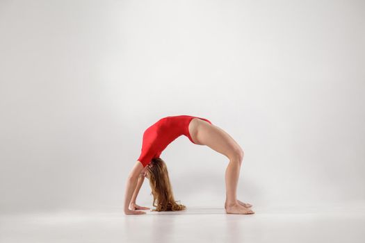 sporty woman balancing on hands and knees and holding back in form of arch while doing bridge urdhva dhanurasana yoga pose. indoor, light gray background. healthy lifestyle and leisure activity.