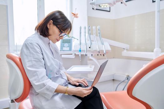 Doctor dentist sitting in the office using a laptop. Dentistry, health care, treatment, work, profession, medicine concept