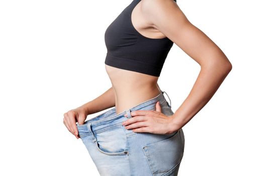 Close-up of slim waist of young woman in big jeans showing successful weight loss, isolated on white background, diet concept.