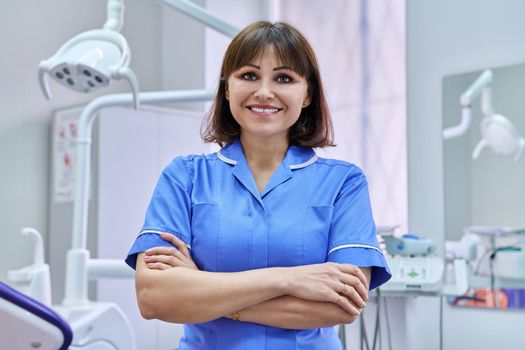 Portrait of smiling nurse looking at camera in dentistry. Confident female with folded hands, dental clinic equipment background. Dentistry, medicine, health care, profession, stomatology concept