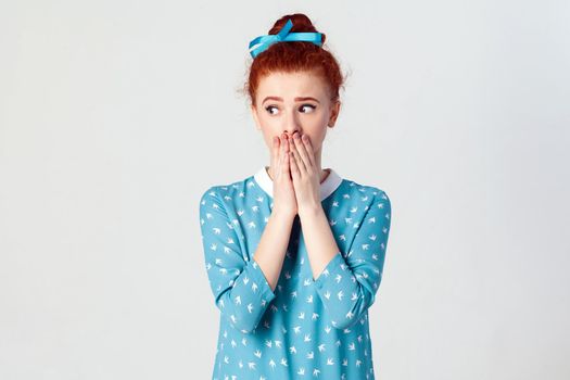The confused young girl. girl covering mouth with both hands keeping a secret. Beautiful redhead girl in blue dress doesn't want to spread rumors or some confidential information.