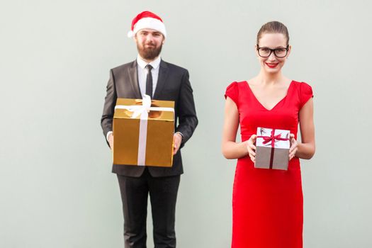 Focus on woman. Couple showing colorful box and smiling. Studio shot, gray wall