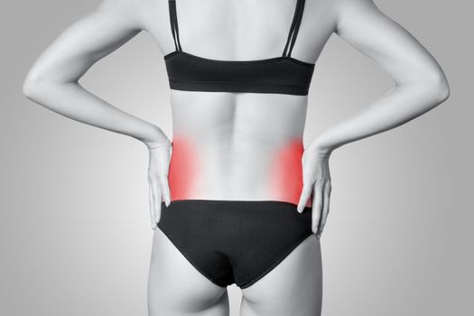 Closeup view of a young woman with pain in kidneys on gray background. Black and white photo with red dot.