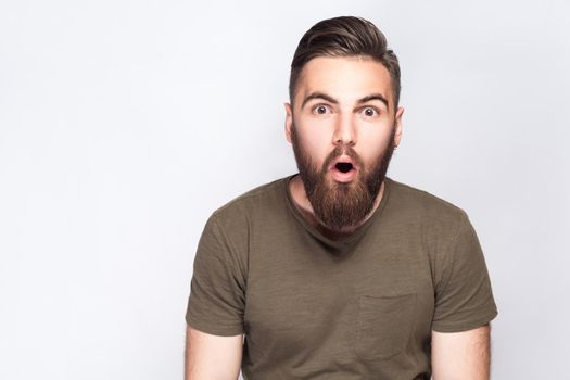 Portrait of surprised bearded man with dark green t shirt against light gray background. studio shot. .