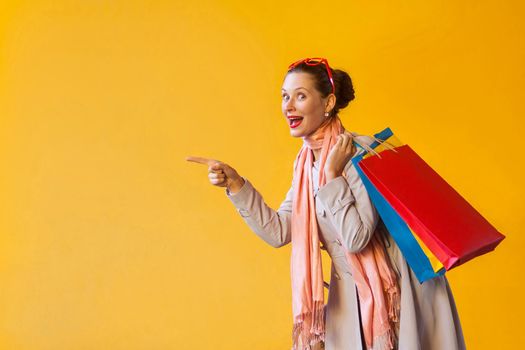 Young adult woman pointing finger on copy space and looking at camera and toothy smile. On yellow background. Studio shot