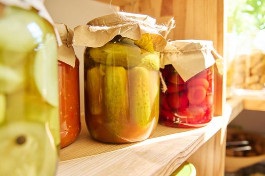 Storage of food in the kitchen in pantry. Pickled canned vegetables and fruits on the shelf, jar of cucumbers close-up. Cooking at home, homemade preservation, household
