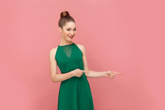 Woman toothy smiling and pointing finger at copy space. Expression emotion and feelings concept. Studio shot, isolated on pink background
