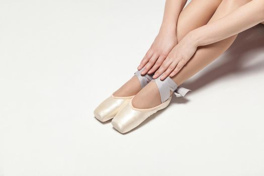 ballerina in pointe shoes sitting on white floor, closeup. indoor, studio shot.