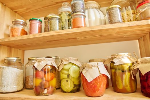 Storage of food in kitchen in pantry. Wooden cabinet with jars and containers, cereals, spices, paste, nuts, canned pickled fruits and vegetables, kitchen utensils. Eat at home, stock food concept