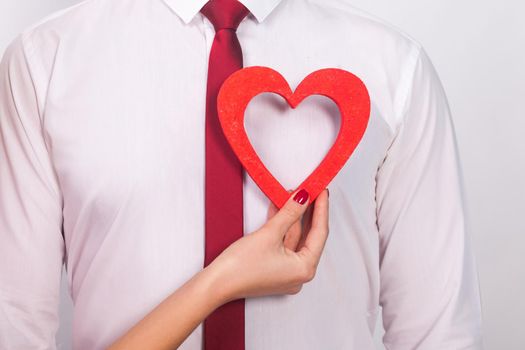 Closeup portrait of unknown man, woman hand , holding his heart. Indoor, studio shot, isolated on gray background