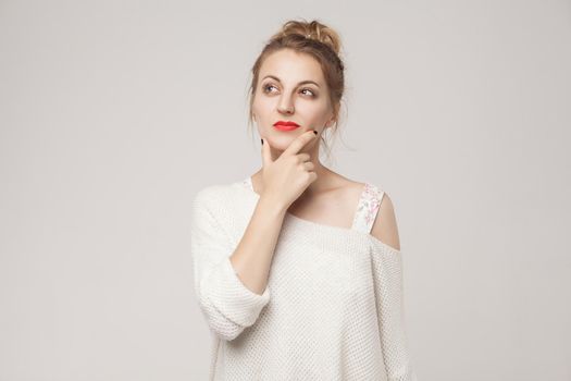 Thoughtful woman touching chin, thinking and looking up . Studio shot, isolated on gray background