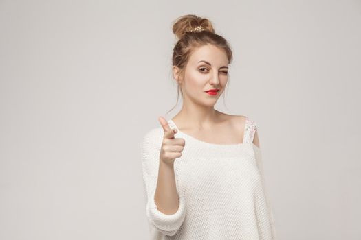 Cute blonde woman wink and pointing finger at camera. Studio shot