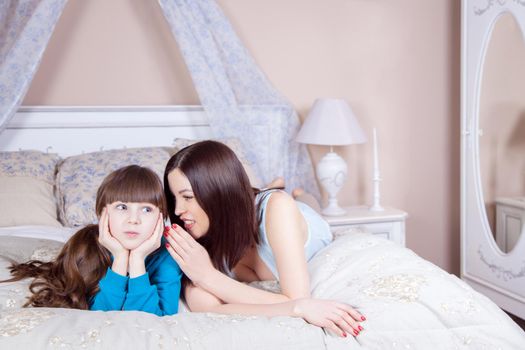 Happy mother and daughter lay in bed having fun, smiling and looking at camera. Studio shot.